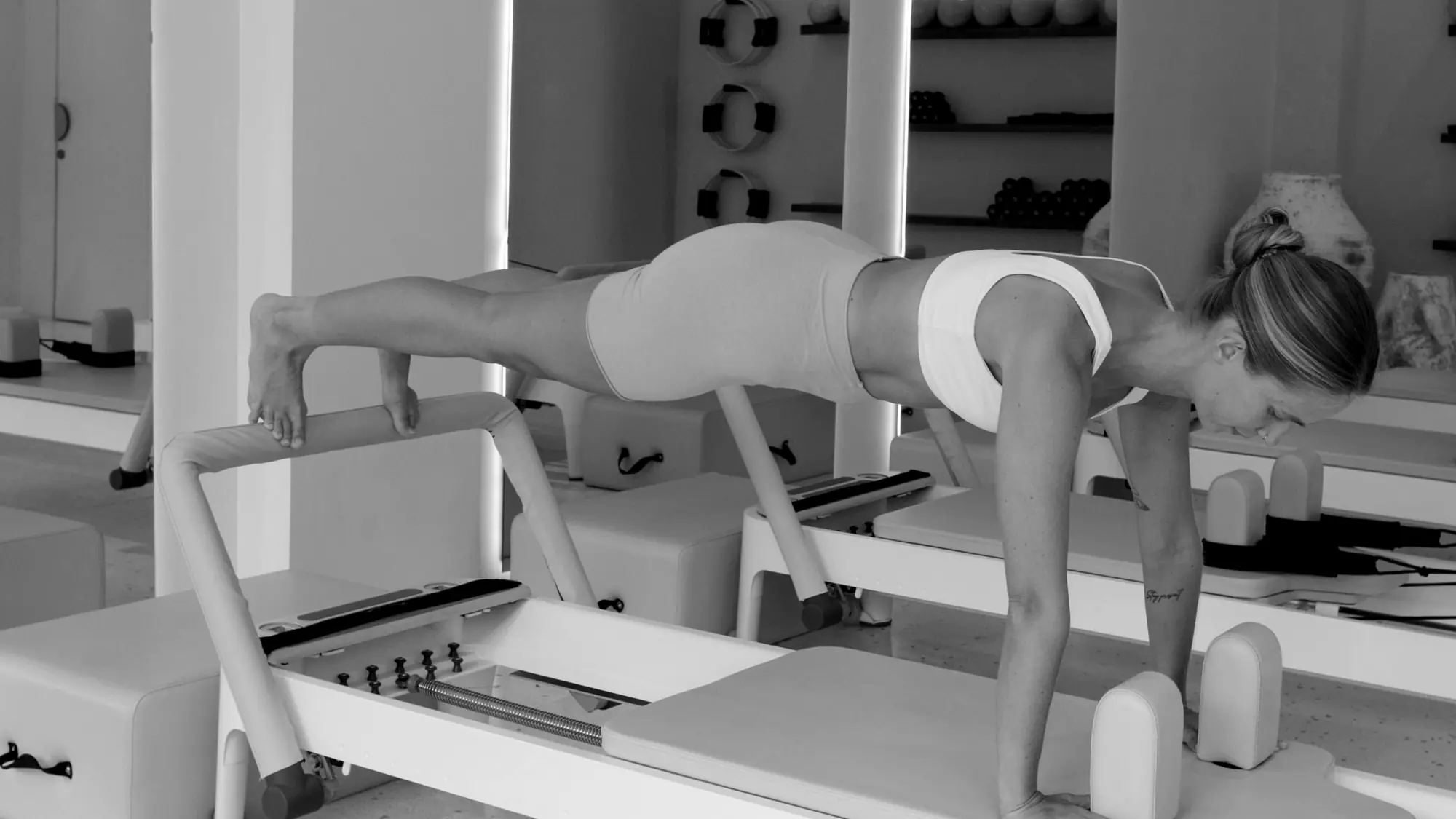 Woman in a plank on a resistance carriage machine in a bright studio