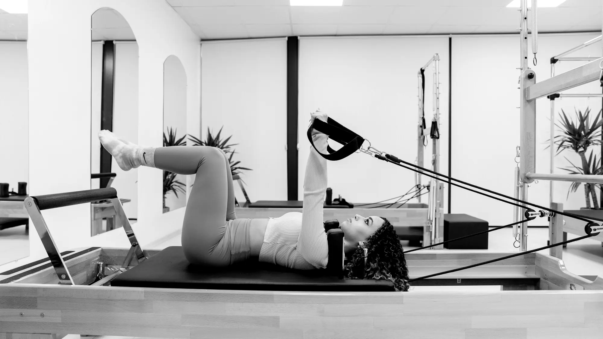 Woman on a Pilates reformer using the straps with her legs lifted