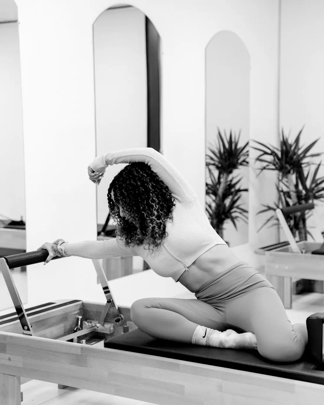 Woman stretching over a Pilates reformer in a bright studio
